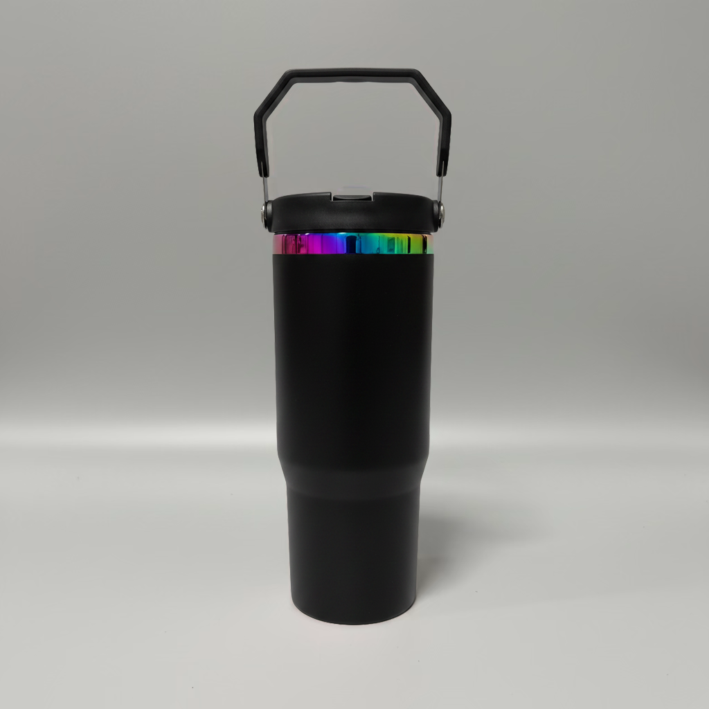 A matte black insulated travel tumbler with a matching black lid and carry handle, featuring a vibrant iridescent rainbow band around the upper portion, set against a neutral gray studio background.