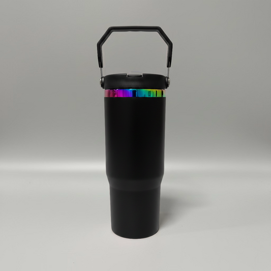 A matte black insulated travel tumbler with a matching black lid and carry handle, featuring a vibrant iridescent rainbow band around the upper portion, set against a neutral gray studio background.