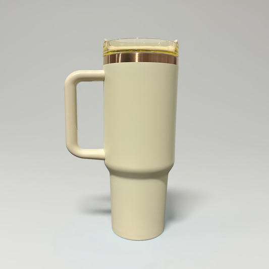 A tall, matte cream-colored travel tumbler with a matching handle and a metallic gold band around the lid, shown on a neutral gray background.