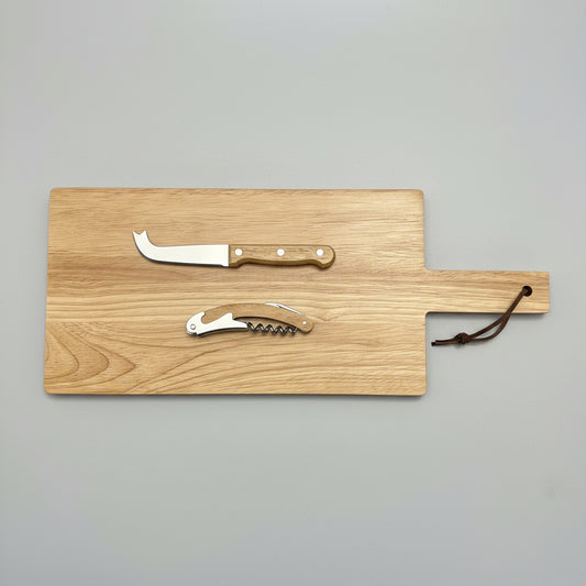A rectangular wooden serving board with a handle, shown on a dark textured surface. The board includes a small cheese knife with a light wood handle and a corkscrew tool attached or displayed on top.